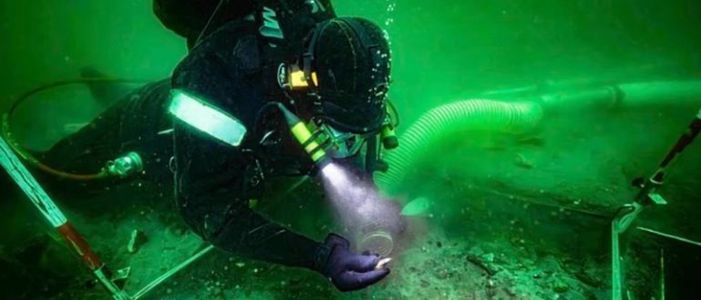 Водолаз с фонарем исследует древние артефакты под водой