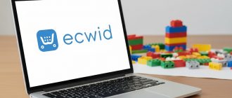 Экран ноутбука с логотипом платформы Ecwid, с разноцветными кубиками на деревянном столе