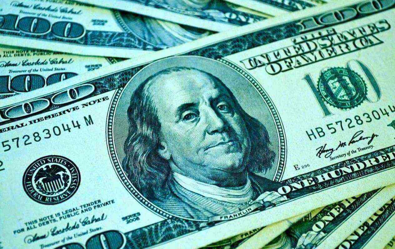 Крупным планом стодолларовая купюра с портретом Франклина на фоне зеленых банкнот.