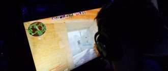 Геймер в наушниках играет в Counter-Strike 2 перед ярким монитором в темной комнате