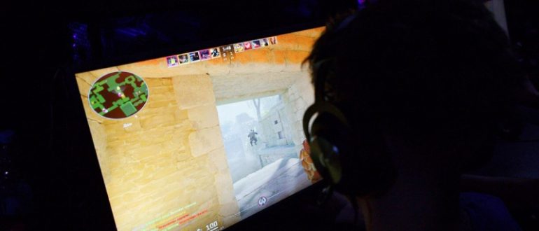 Геймер в наушниках играет в Counter-Strike 2 перед ярким монитором в темной комнате